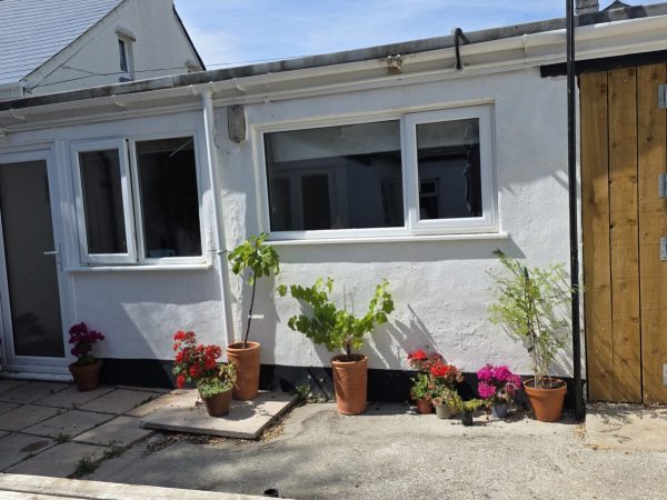 An outside view of the single-story Bed and Breakfast accommodation with its big windows cheerful flowerpots and white walls